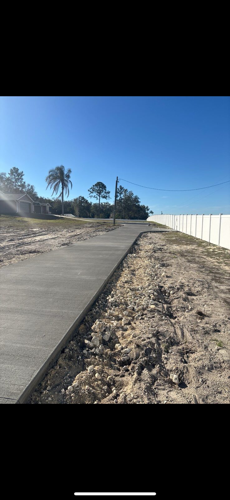 Long concrete sidewalk pour next to white vinyl fence